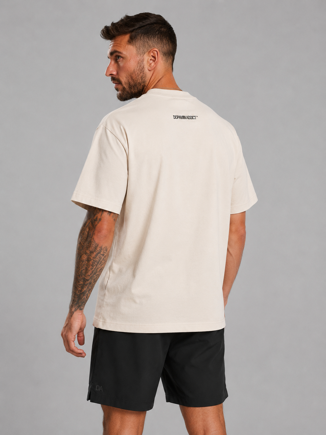 Man wearing a beige t-shirt with a logo on the back against a gray background